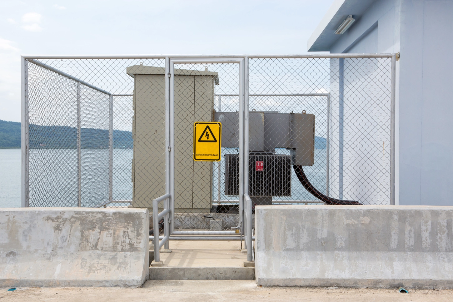 Veilig omheinde buiteninstallatie van een prefabhoogspanningscabine aan het water met waarschuwingsbord